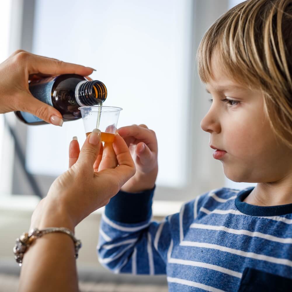 Kind das auf einen Messbecher zeigt, in den Sirup von einer Frau eingegossen wird.